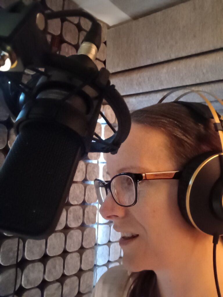 Rebecca in her audio booth wearing headphones and facing a microphone
